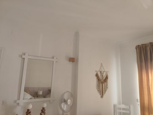 Quarto luminoso da Albufeira Inn com paredes brancas, espelho decorativo, painel de macramé e ventilador