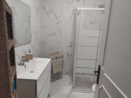 Banheiro moderno da Albufeira Inn com revestimento efeito mármore, pia branca, box de banho e toalheiro aquecido