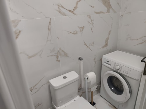 Banheiro da Albufeira Inn com azulejos efeito mármore, vaso sanitário, bidê, máquina de lavar e suporte para escova de vaso