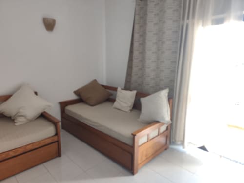 Dois camas de solteiro em madeira com almofadas brancas e cortinas cinzentas no quarto da Albufeira Inn, iluminação natural abundante da porta da varanda