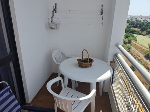 Varanda ensolarada com mesa de jantar branca e cadeiras na Albufeira Inn, com vista para jardins verdes e área residencial