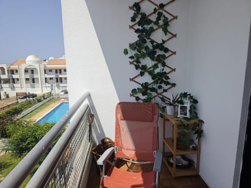 Terraço da varanda do Albufeira Inn com cadeira vermelha, treliça com hera, vista da piscina e guarda-corpos brancos