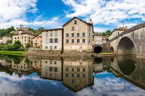 Pont de pierre médiéval et bâtiments historiques reflétés dans l'eau calme aux Murmures du Bois, Sousceyrac-en-Quercy