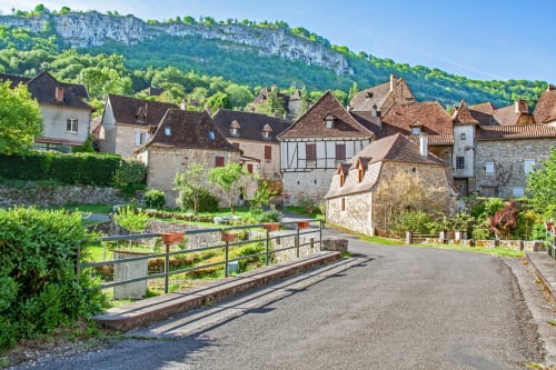 Village médiéval de Sousceyrac-en-Quercy aux bâtiments en pierre, pont et falaises calcaires en arrière-plan.