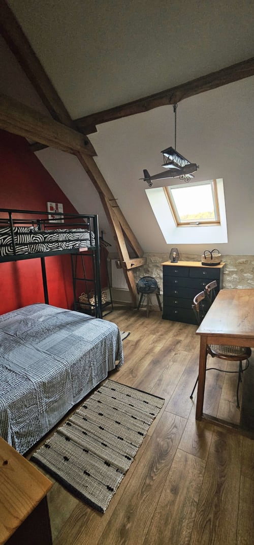 Chambre mansardée aux Granges Indigo avec lit mezzanine, poutres apparentes, lucarne, commode noire et mobile avion