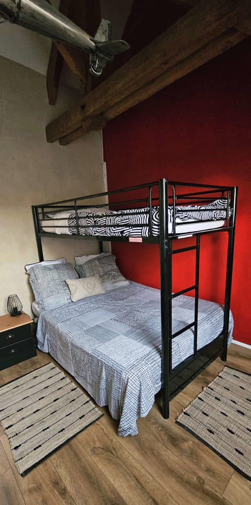 Lit superposé en métal noir avec matelas à rayures zèbres dans le gîte Les Eyzies aux Granges Indigo, mur d'accent rouge, bois apparent