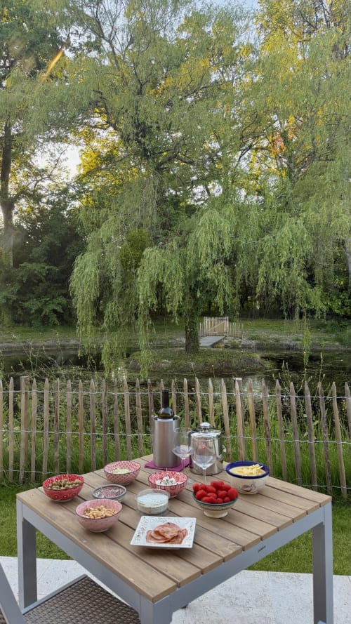 Outdoor picnic table laden with appetizers and drinks overlooking a lake with weeping willow trees at Cloffy cottage in