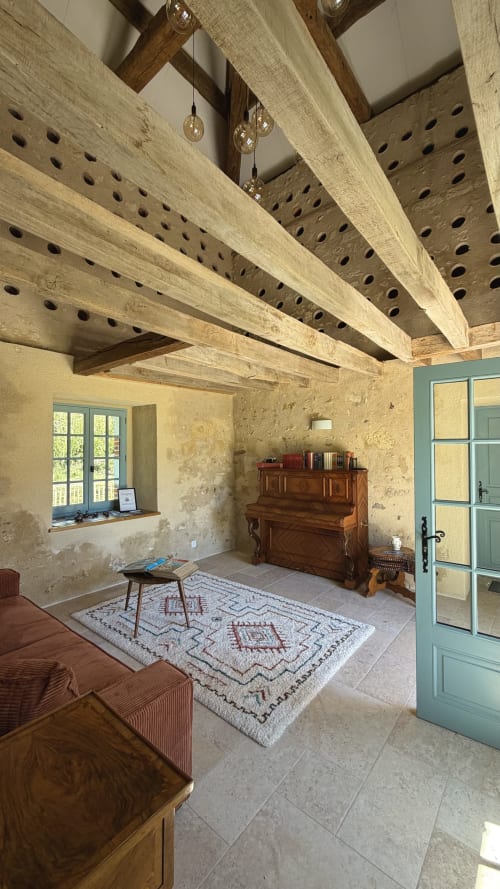 Intérieur rustique du gîte Cloffy avec poutres apparentes, murs en pierre, piano et porte turquoise