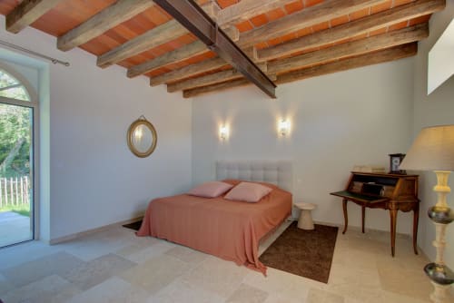 Chambre rustique au Cloffy avec poutres apparentes, lit en terre cuite, bureau en bois et accès à la vue sur le lac.