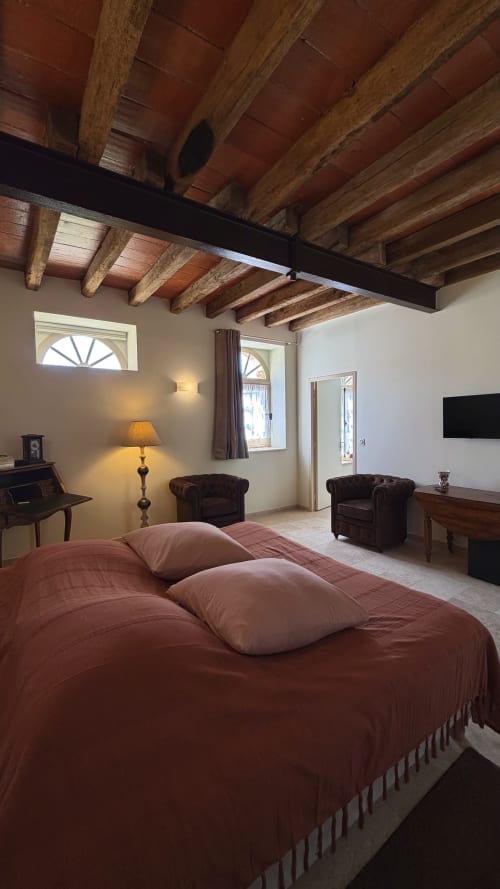 Chambre rustique avec poutres en bois apparentes, linge terracotta et mobilier d'époque au cottage Cloffy