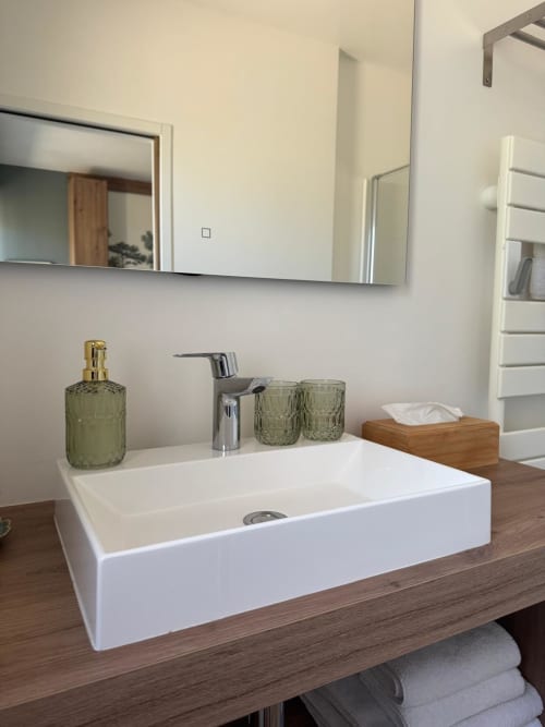 Modern bathroom vanity with white rectangular sink, green glass accessories, and wood countertop at Les clés d'à côté near