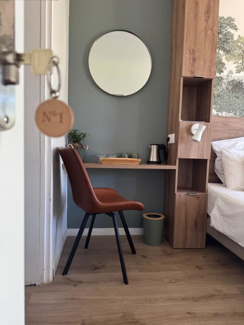 Modern bedroom desk area with rust-colored chair, round mirror, and wooden storage at Les clés d'à côté guesthouse near