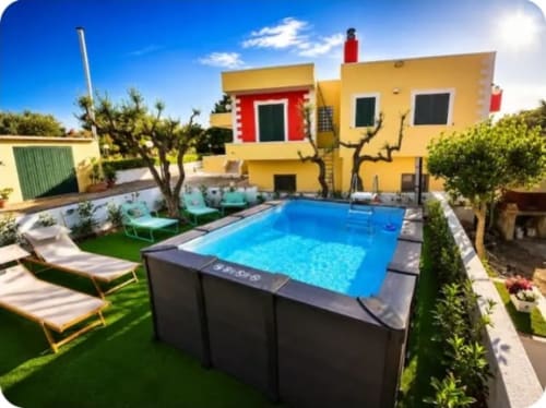 Dimora Pierino villa in Martina Franca with yellow facade, blue pool, lounge chairs, and lush garden courtyard