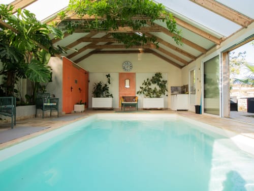 Piscine intérieure chauffée à L'Ecrin des Roches B&B au Langon, avec verrière, poutres bois, plantes en pots et porte orange