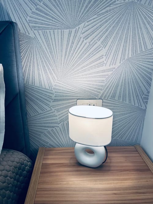 Elegante lampada bianca su tavolo in legno nella camera da letto Anima Est Napoli con carta da parati a righe blu