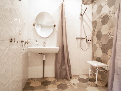 Salle de bains accessible à L'Ecrin des Roches : lavabo, miroir, douche avec barres de soutien et siège