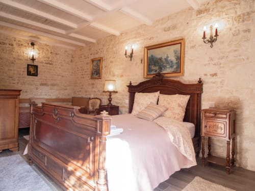 Chambre élégante à L'Écrin des Roches avec mobilier en bois, murs en pierre et literie rose au Langon