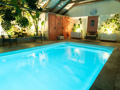 Piscine intérieure de L'Ecrin des Roches B&B au Langon, entourée de plantes tropicales et de chaises longues
