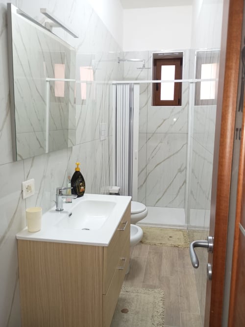 Moderno bagno in Camera Sophie presso B&B S HOME Napoli, con piastrelle in marmo, box doccia in vetro e mobile lavabo in legno