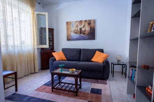 Elegante soggiorno con divano blu navy, cuscini arancioni, tavolino in legno e quadri alle pareti nell'appartamento fronte mare di Marsaskala