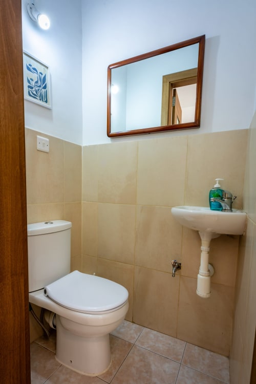Bagno pulito nella casa in prima linea a Marsaskala con toilet, lavabo a colonna, specchio e pareti in piastrelle beige