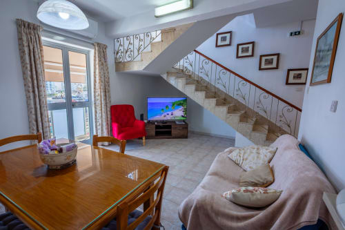 Luminosa zona giorno al fronte mare con tavolo da pranzo, poltrona rossa, TV, divano beige e scala decorativa