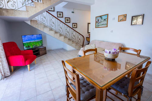 Ampio soggiorno con tavolo da pranzo, poltrona rossa, TV e scala nella townhouse fronte mare di Marsaskala