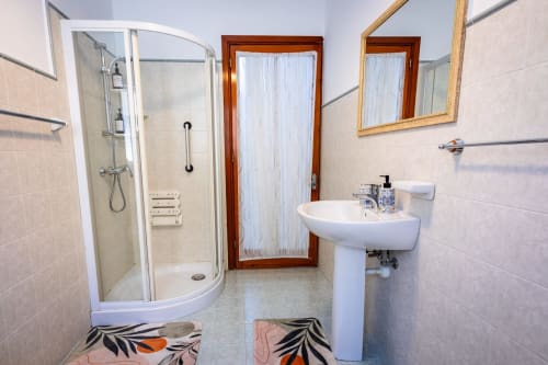 Bagno moderno con doccia curva, lavabo su colonna e tappeti decorativi nella villa sul mare di Calm Holiday Homes