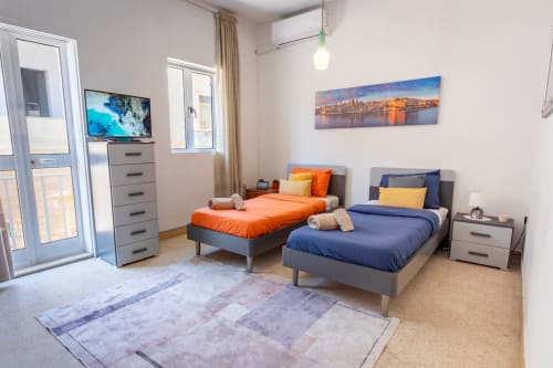 Camera da letto moderna con due letti arancioni e blu, TV e quadri con veduta della città a Marsaskala Seafront