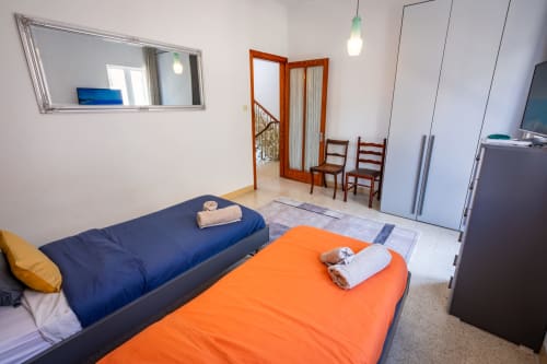 Camera da letto luminosa con letti blu e arancioni, specchio, guardaroba e sedie in legno nella townhouse fronte mare di Marsaskala