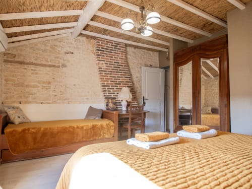 Chambre Deluxe jaune à L'Ecrin des Roches avec murs en pierre apparente, poutres en bois, lit queen-size et lit de repos à Le Langon, France