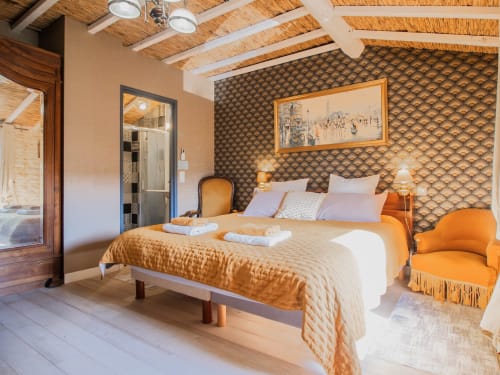 Chambre déluxe à L'Ecrin des Roches avec accents orange, tête de lit motifs, poutres bois et salle de bain attenante