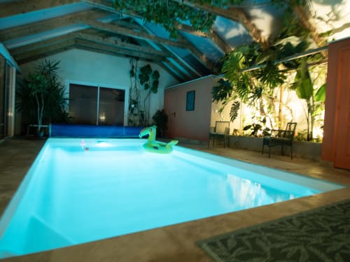 Piscine intérieure illuminée à L'Ecrin des Roches avec transat vert, plantes en pot et espace lounge couvert