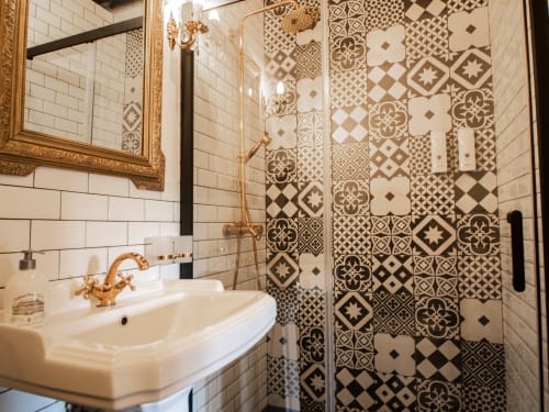Salle de bain luxueuse à L'Ecrin des Roches avec carrelage à motifs ornementaux, murs en carrelage blanc, robinetterie dorée et douche spacieuse