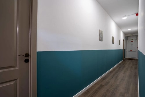 Corredor moderno do Madeirarooms Funchal com paredes em tons de azul-petróleo e branco, piso em madeira e iluminação contemporânea