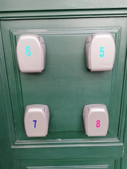 Quatro caixas de chaves Master Lock brancas numeradas 5, 6, 7, 8 montadas em porta verde no hotel Madeirarooms, Funchal
