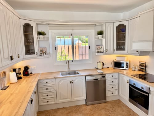 Cocina moderna con muebles blancos, encimeras de madera, electrodomésticos de acero inoxidable y vistas al mar en Villa Sienna, Nerja