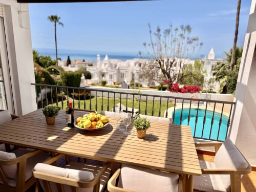 Soleado balcón de Villa Sienna en Nerja con mesa de comedor, vistas al mar Mediterráneo, piscina y edificios encalados
