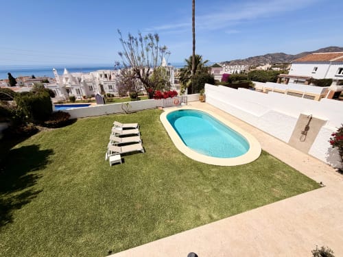 Villa Sienna en Nerja: piscina privada, tumbonas blancas en jardín cuidado, vista al mar Mediterráneo, ubicada en ladera costera