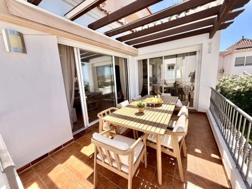 Terraza soleada en Villa Sienna de Nerja con mesa de comedor de madera, tumbonas, pérgola y vistas al mar de la costa.