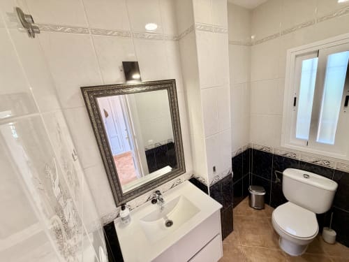 Baño moderno en Villa Sienna Nerja con lavamanos blanco, espejo enmarcado, detalles en azulejos negros e inodoro