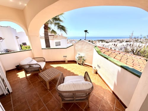 Soleada terraza de Villa Sienna en Nerja con asientos de mimbre, vistas al mar y paisaje costero mediterráneo