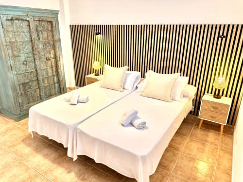 Dormitorio en Villa Sienna, Nerja con ropa de cama blanca, almohadas rosas, cabecero rayado, armario de madera y suelo de terracota