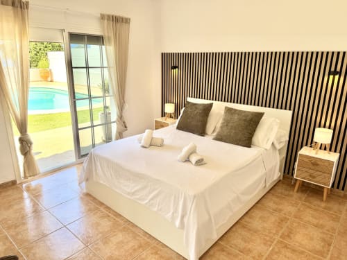 Dormitorio moderno en Villa Sienna, Nerja con cabecero rayado, vista a piscina a través de puertas de cristal y suelos de terracota