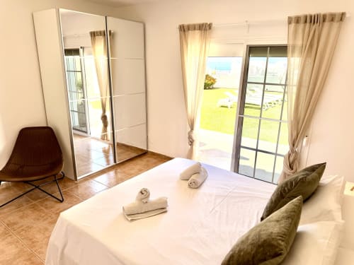 Luminoso dormitorio de villa en Nerja con vistas al mar, armario espejo, cama blanca, zona de descanso y acceso al jardín