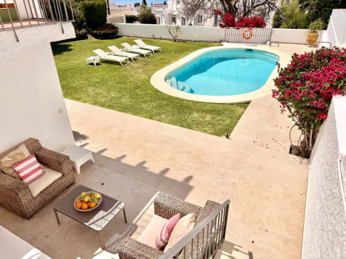 Villa Sienna Nerja: Jardín trasero de lujo con piscina turquesa, tumbonas, flores vibrantes y zona de descanso en terraza