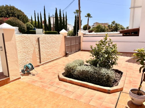 Amplia terraza de Villa Sienna en Nerja con baldosas de terracota, macetas y cipreses visibles más allá del muro