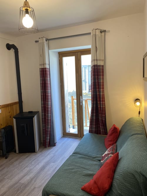 Chambre cosy de L'encabanée avec lit vert, coussins rouges, cheminée et balcon vue sur la ville à Saint-Paul-sur-Ubaye
