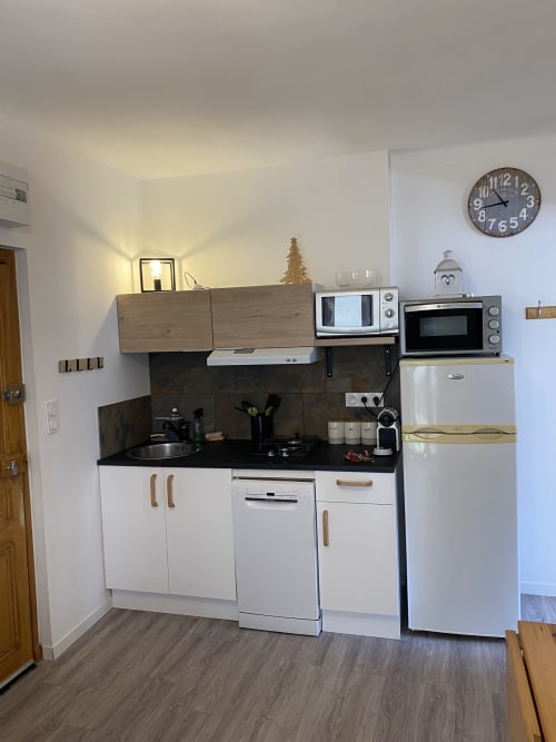 Petite cuisinette du gîte L'encabanée avec meubles blancs, plan de travail noir, électroménager et détails en bois