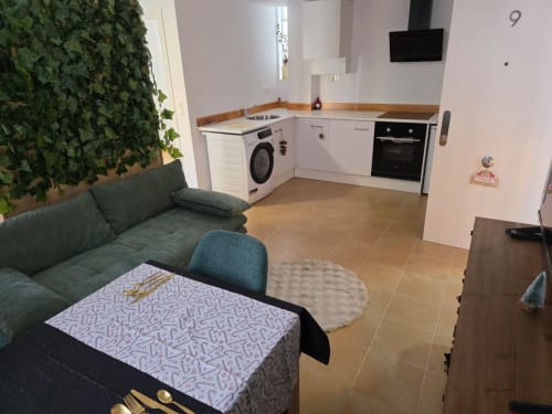 Cocina abierta y salón moderno en Apartamentos el Manantial de Chóvar con sofá verde, mesa de comedor y electrodomésticos